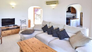 A living room with a sofa, a wooden coffee table, a TV on a wooden stand, and a kitchen visible through an archway. - Villa Clementina by Interhome (Pego)