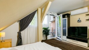 A bedroom with a bed, a TV, a plant, and a balcony with a chair.