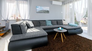A modern living room with a sectional sofa, a small round table, and a large window with sheer curtains.