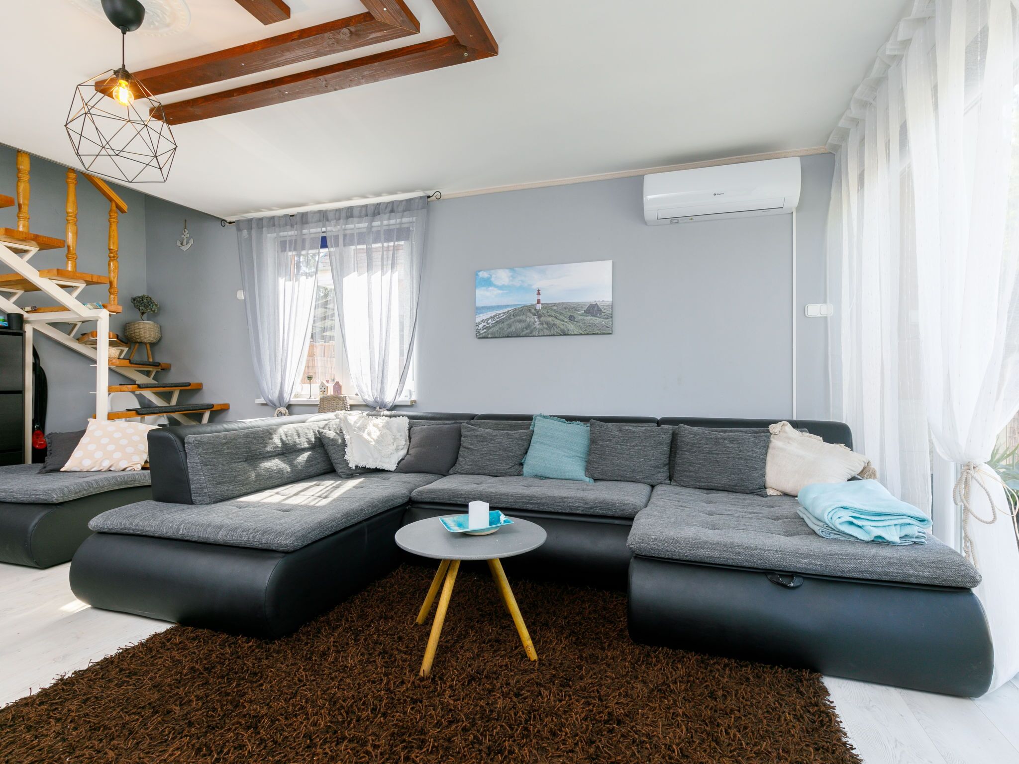 A modern living room with a sectional sofa, a small round table, and a staircase with wooden railings.