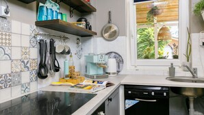 A kitchen with a black stove, a dishwasher, a window with a view of greenery, and various kitchen utensils and appliances.