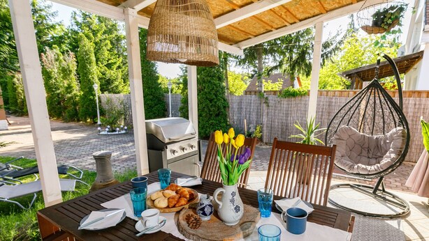 An outdoor patio with a wooden table set for a meal, surrounded by chairs and a hanging chair.