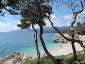 Un paysage côtier avec une eau bleue et limpide, une côte rocheuse et quelques personnes sur la plage.