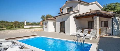 A two-story house with a swimming pool and white lounge chairs.