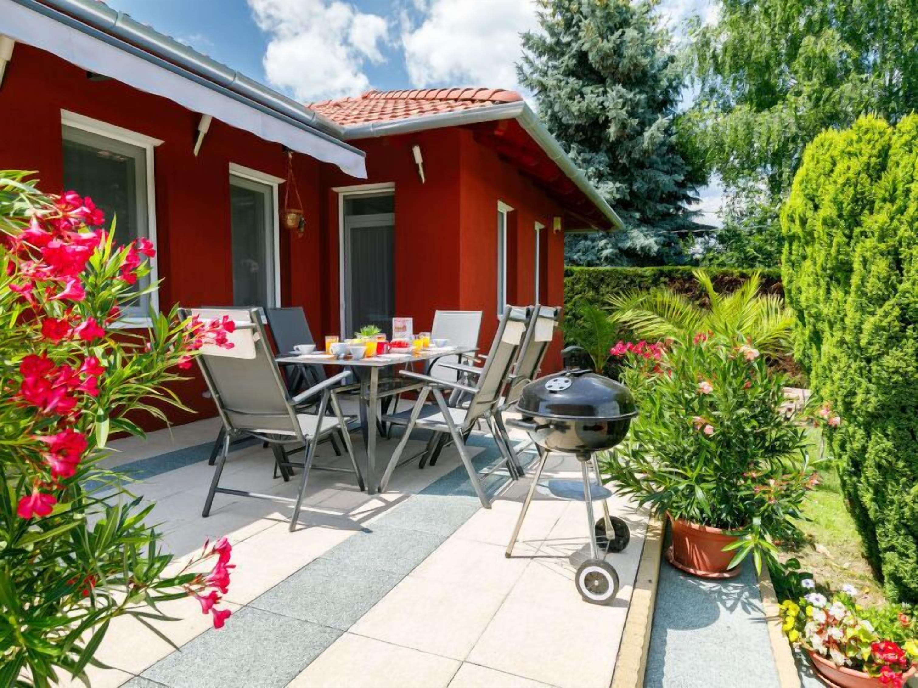 Un edificio rojo con techo de tejas, un patio con mesa y sillas, y una parrilla.