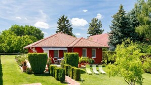 Una casa roja con tejado de tejas, rodeada de céspedes y setos bien cuidados.
