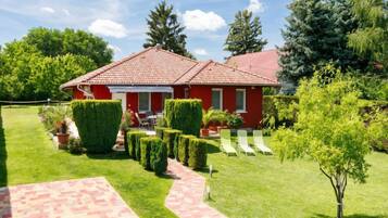Une maison rouge avec un toit en tuiles, entourée de pelouses et de haies bien entretenues.