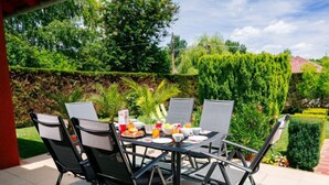 Un patio con una mesa dispuesta para el desayuno, rodeada de sillas y vistas a un jardín.