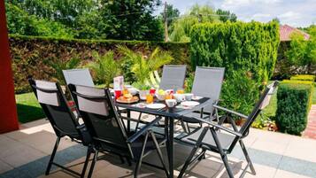 Une terrasse avec une table dressée pour le petit-déjeuner, entourée de chaises, donnant sur un jardin.