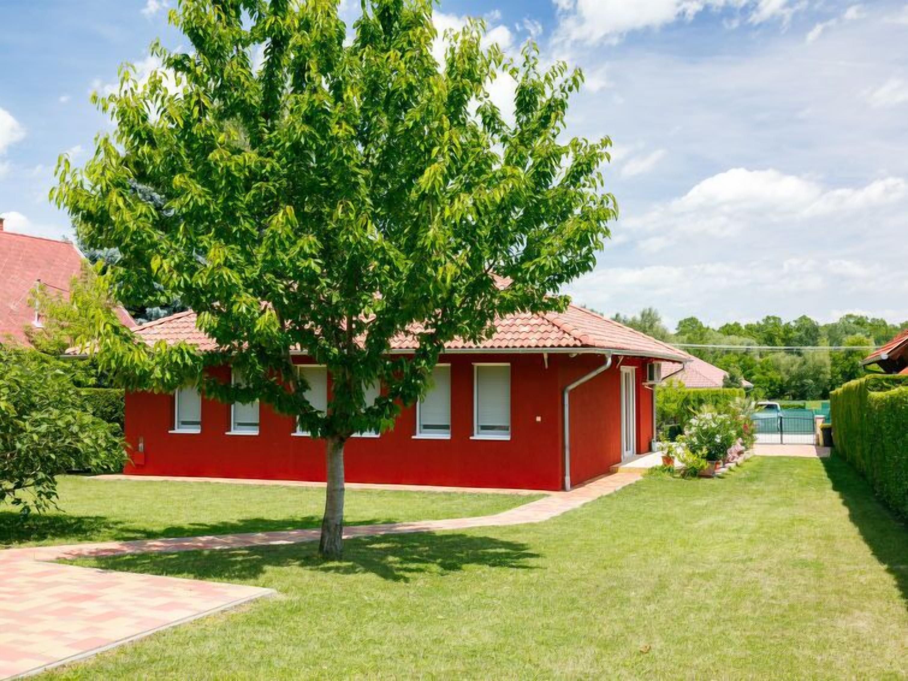 A red building with a tiled roof, surrounded by a well-maintained lawn and a large tree.