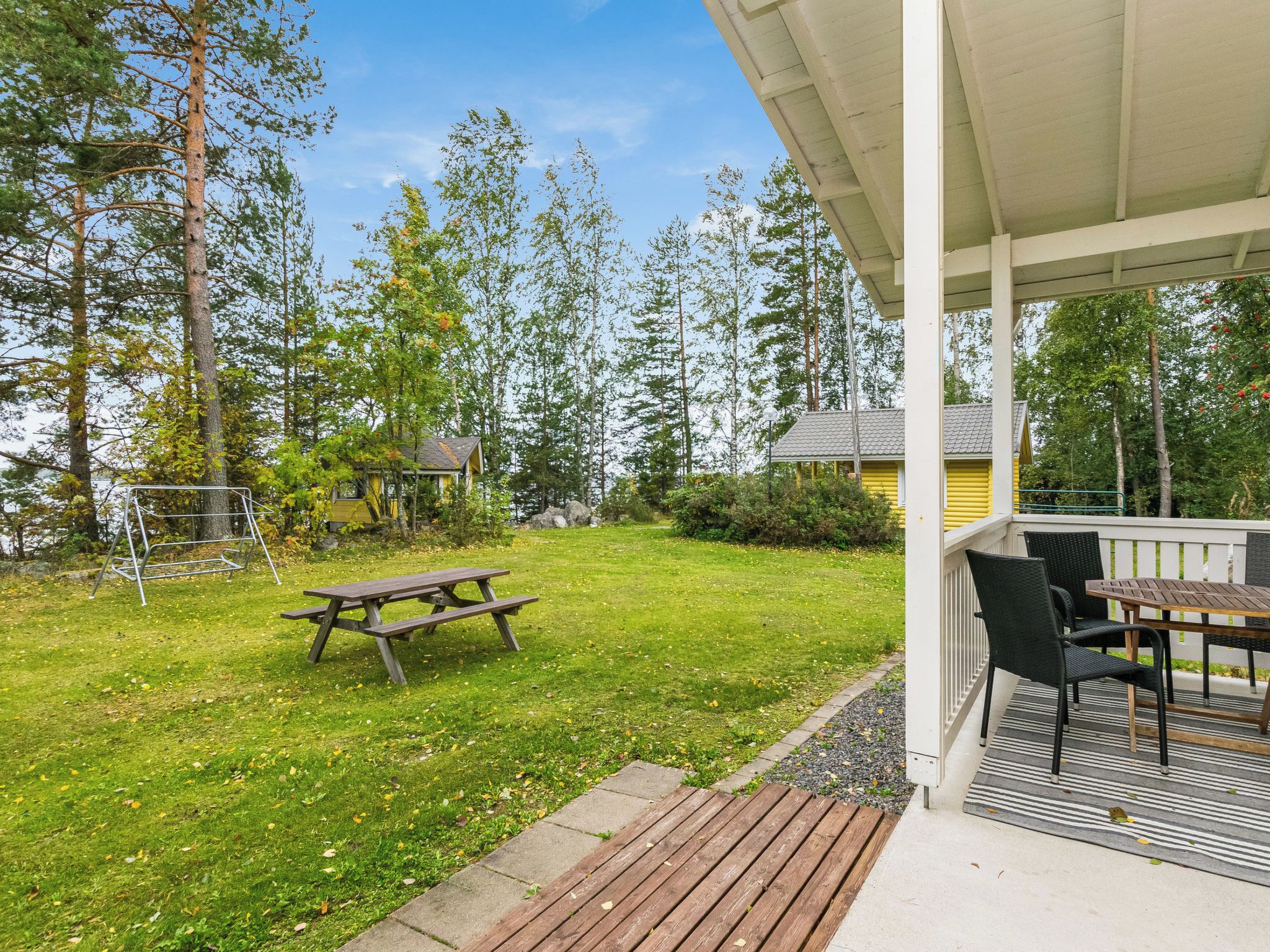A covered outdoor area with a picnic table and chairs, surrounded by a grassy lawn and trees.