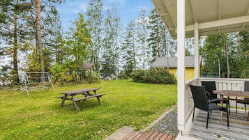 A covered outdoor area with a picnic table and chairs, surrounded by a grassy lawn and trees.