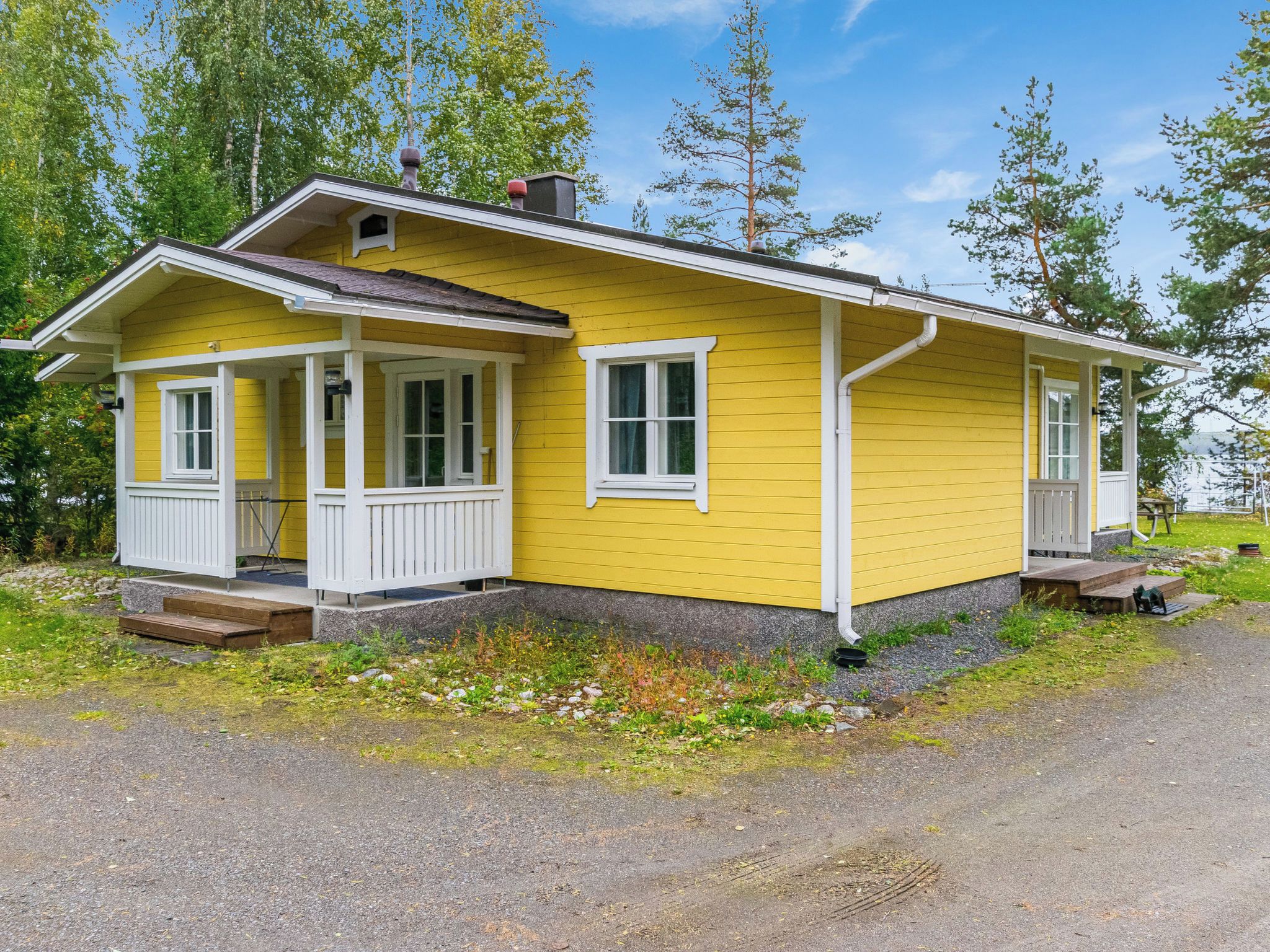 A yellow house with a porch and a chimney.