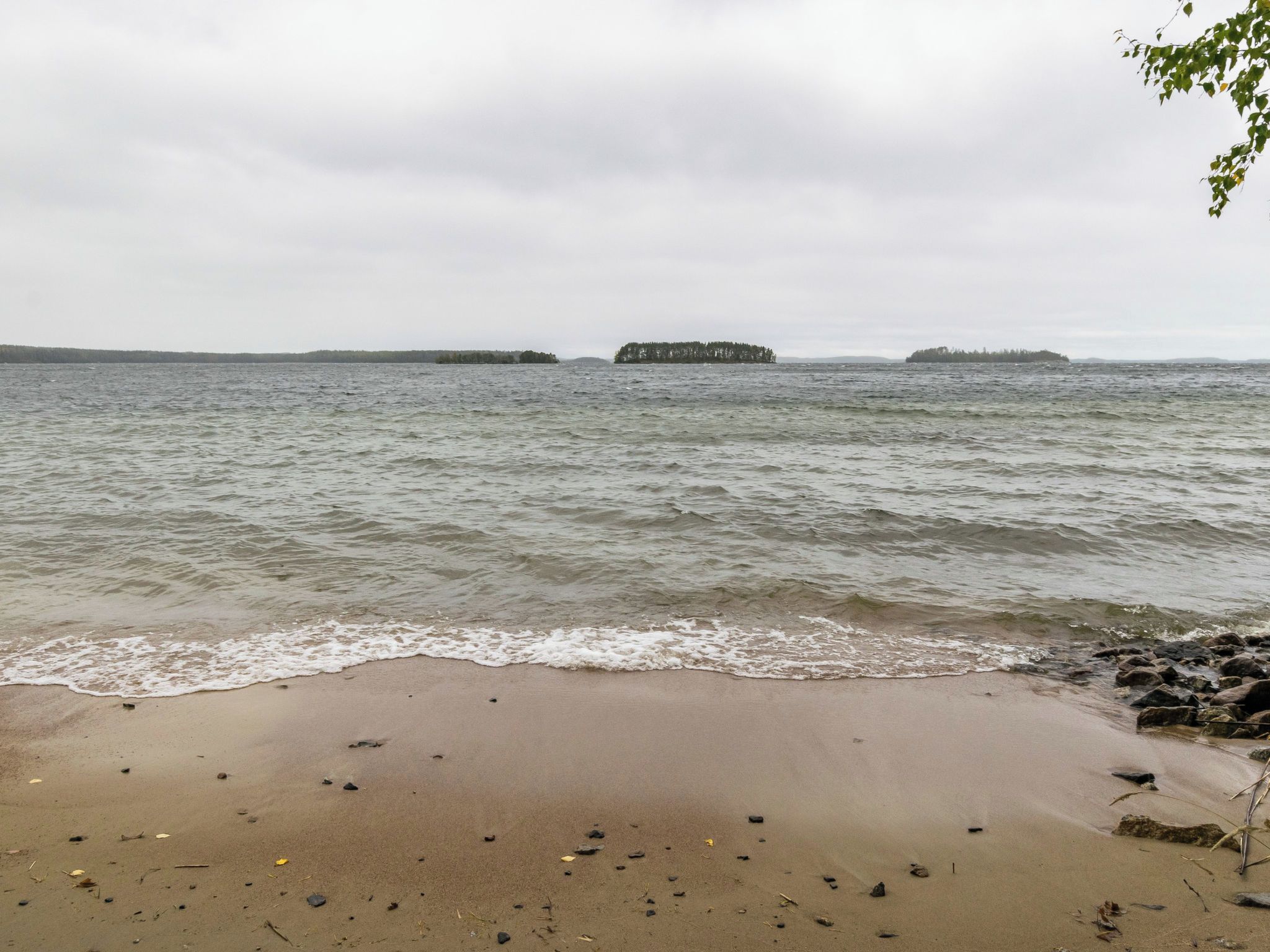 Una playa con aguas tranquilas, una orilla arenosa y islas a lo lejos.