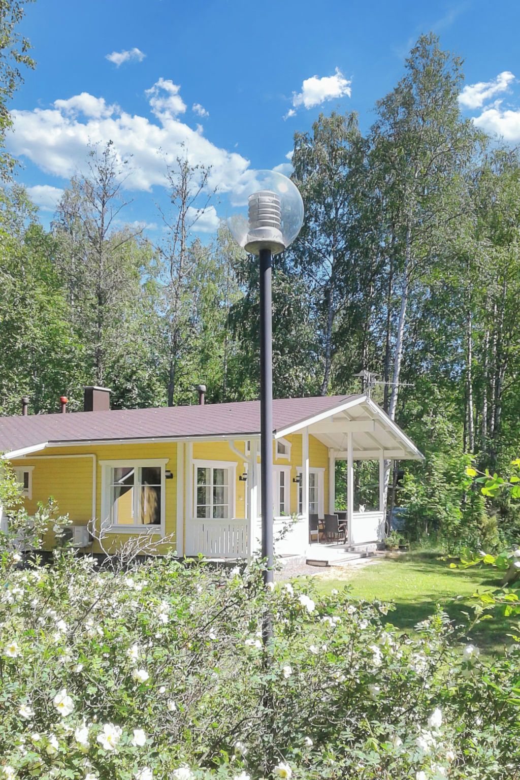 Una casa amarilla con porche, rodeada de árboles y un cielo despejado.