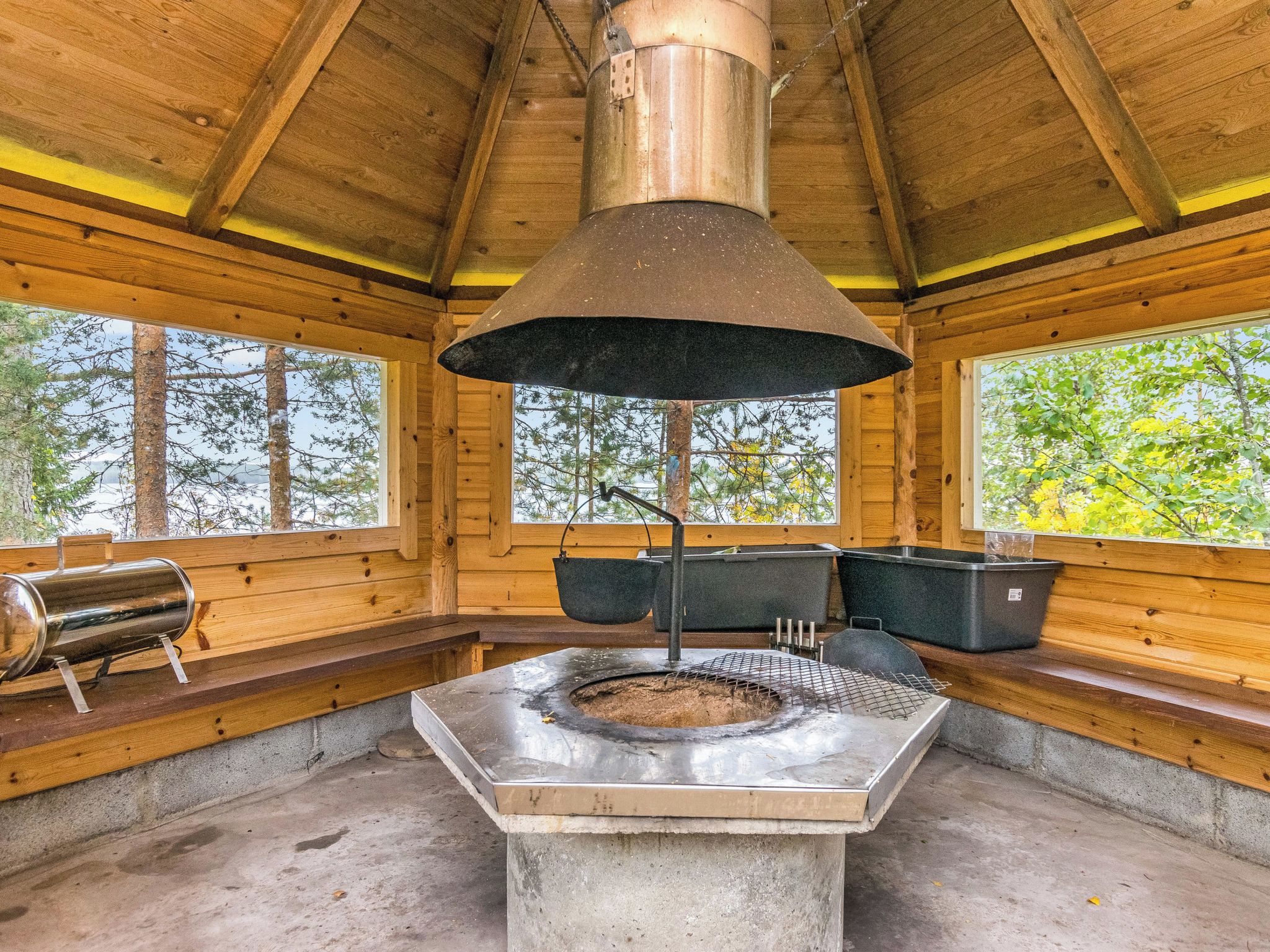 A rustic wooden cabin with a large stone fireplace, benches, and a hanging pot rack.