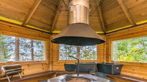 Una cabaña rústica de madera con chimenea de piedra central, ventanas grandes y una chimenea.