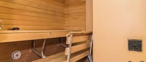 A sauna room with wooden benches and a metal grate on the floor.