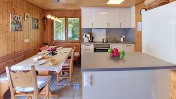 A wooden interior with a dining table, chairs, a kitchen with white cabinets, and a refrigerator.