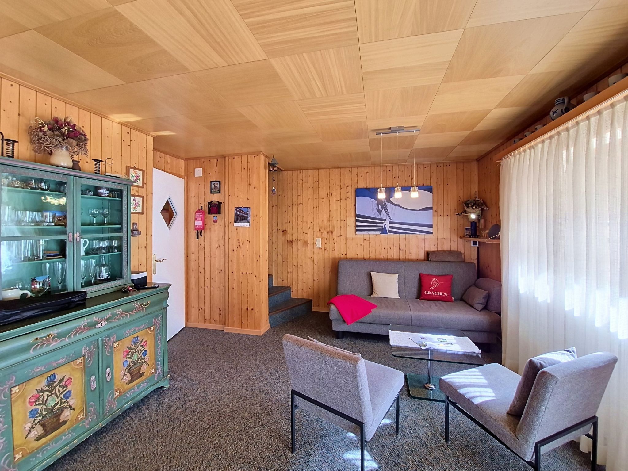 A cozy room with a wooden interior, a sofa, a glass coffee table, and a cabinet with glass doors.