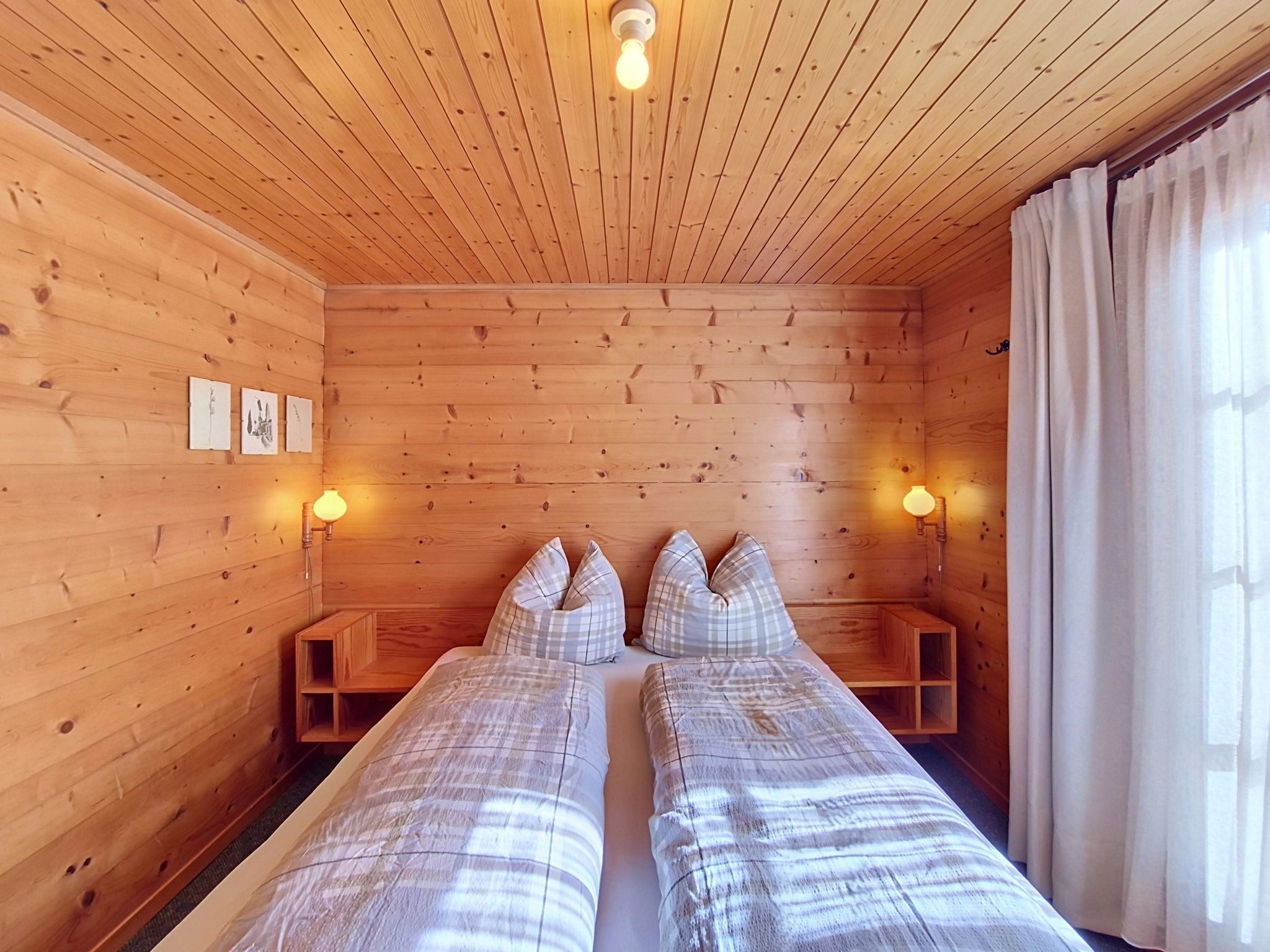 A wooden cabin room with two beds, two bedside lamps, and a window with curtains.