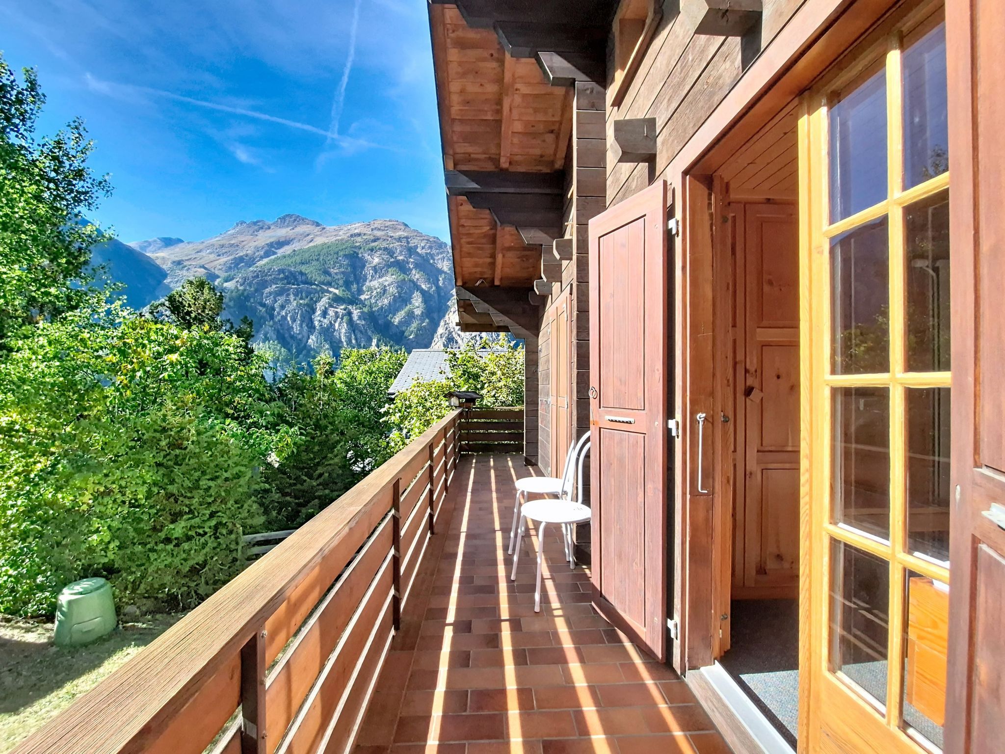 A wooden balcony with a view of mountains, a wooden door, and a small table with chairs.