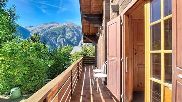 A wooden balcony with a view of mountains, a wooden door, and a small table with chairs.