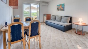A room with a dining table, chairs, a sofa, a small side table with a lamp, and a painting on the wall.