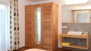 Une chambre à coucher avec un lit, une armoire en bois, une salle de bain avec un lavabo et un miroir.