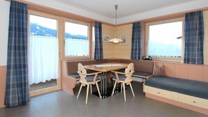 Une pièce de taille modeste comprenant une table et des chaises, un banc et de grandes fenêtres avec des rideaux.