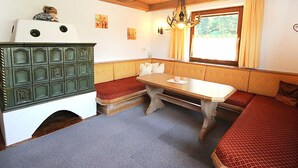 Une pièce chaleureuse avec des poutres en bois, un banc servant de coin salon, une table et un meuble vert.