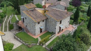 Um edifício de pedra com várias divisões, rodeado por um jardim bem cuidado e colinas arborizadas.
