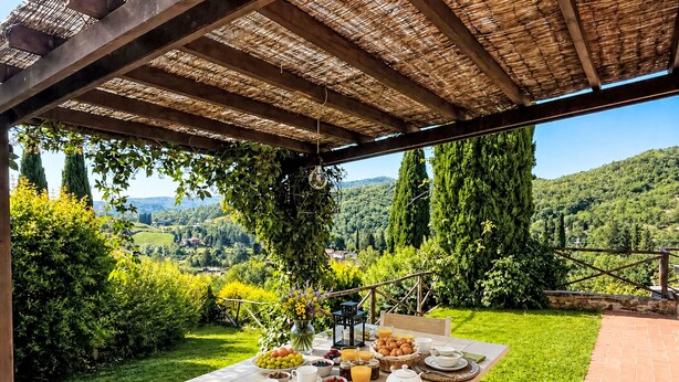 Área de refeições ao ar livre com mesa posta para o café da manhã, rodeada por vegetação exuberante e uma vista panorâmica.