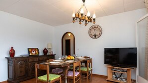 Un comedor con una mesa de madera, sillas, una araña, un reloj y un televisor sobre un mueble.