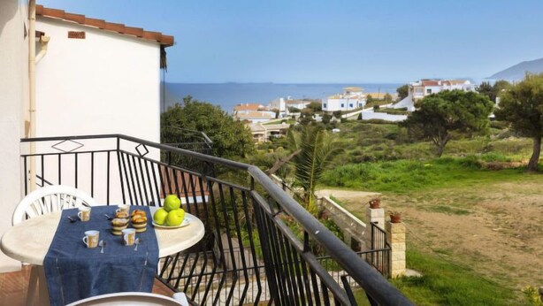 Un balcón con una mesa lista para el desayuno, con vistas a un pueblo costero y al mar.