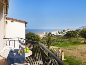 Un balcone con un tavolo apparecchiato per la colazione, vista su una cittadina costiera e il mare.
