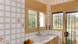 Una cocina con paredes de azulejos blancos, un mueble de madera, un lavamanos y una ventana con vistas a zonas verdes.