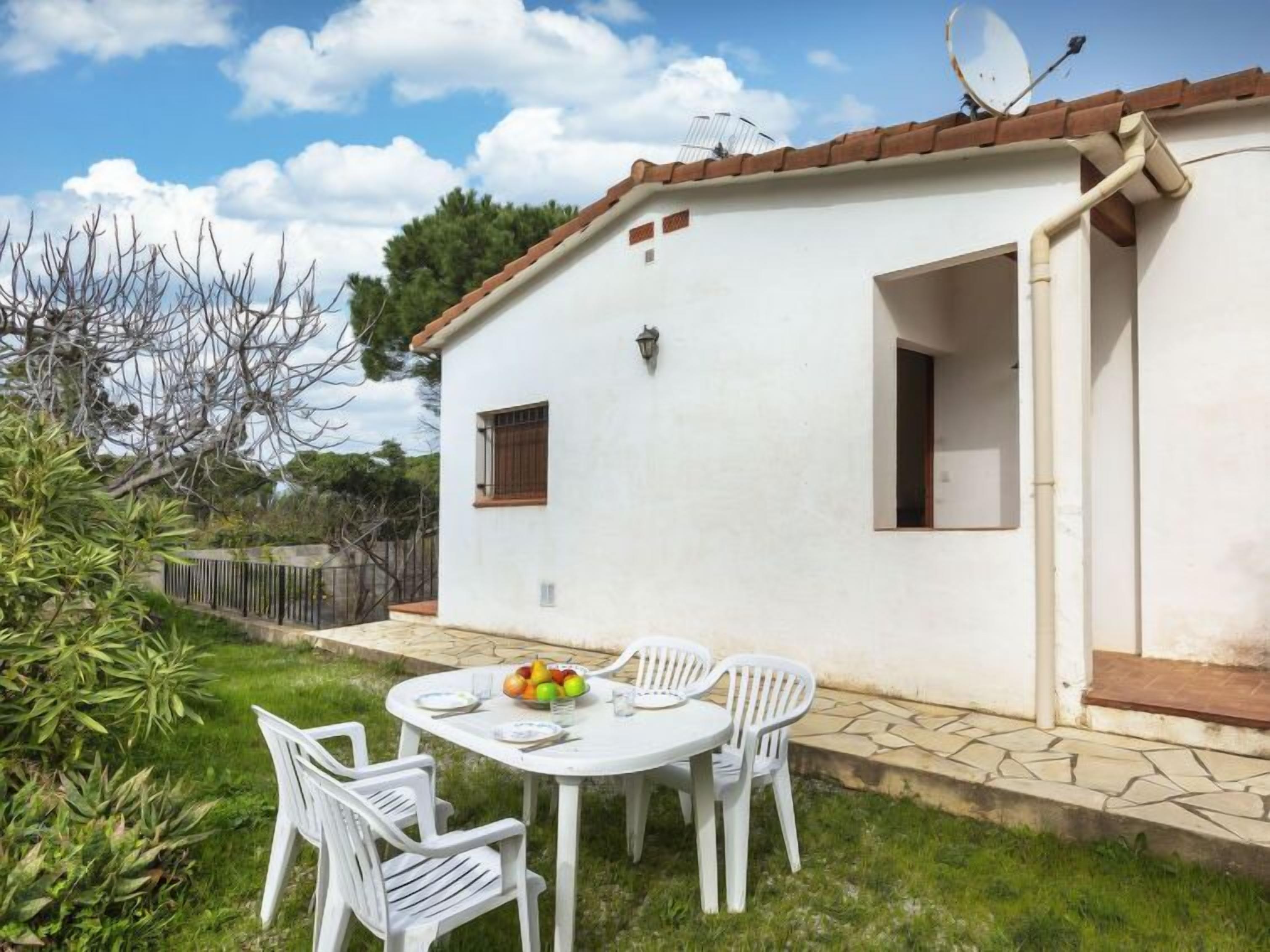 Une maison blanche avec un toit en tuiles, une antenne parabolique et un petit jardin avec une table et des chaises.