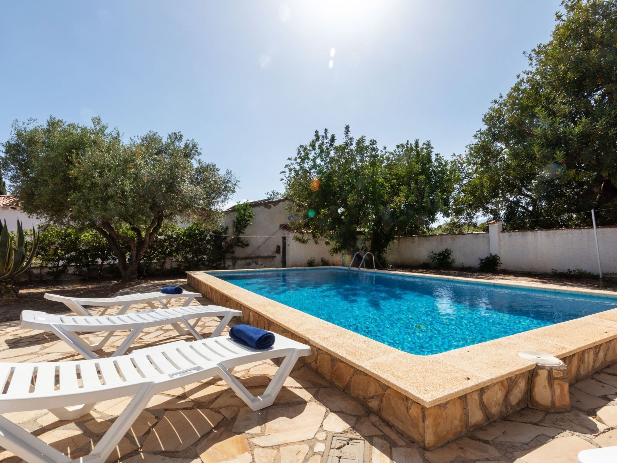 Une piscine rectangulaire bordée de pierres, entourée de chaises longues blanches et d’une terrasse en pierre.