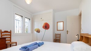 Un dormitorio con una cama, una silla, un escritorio, un espejo y una ventana con una reja decorativa de metal.