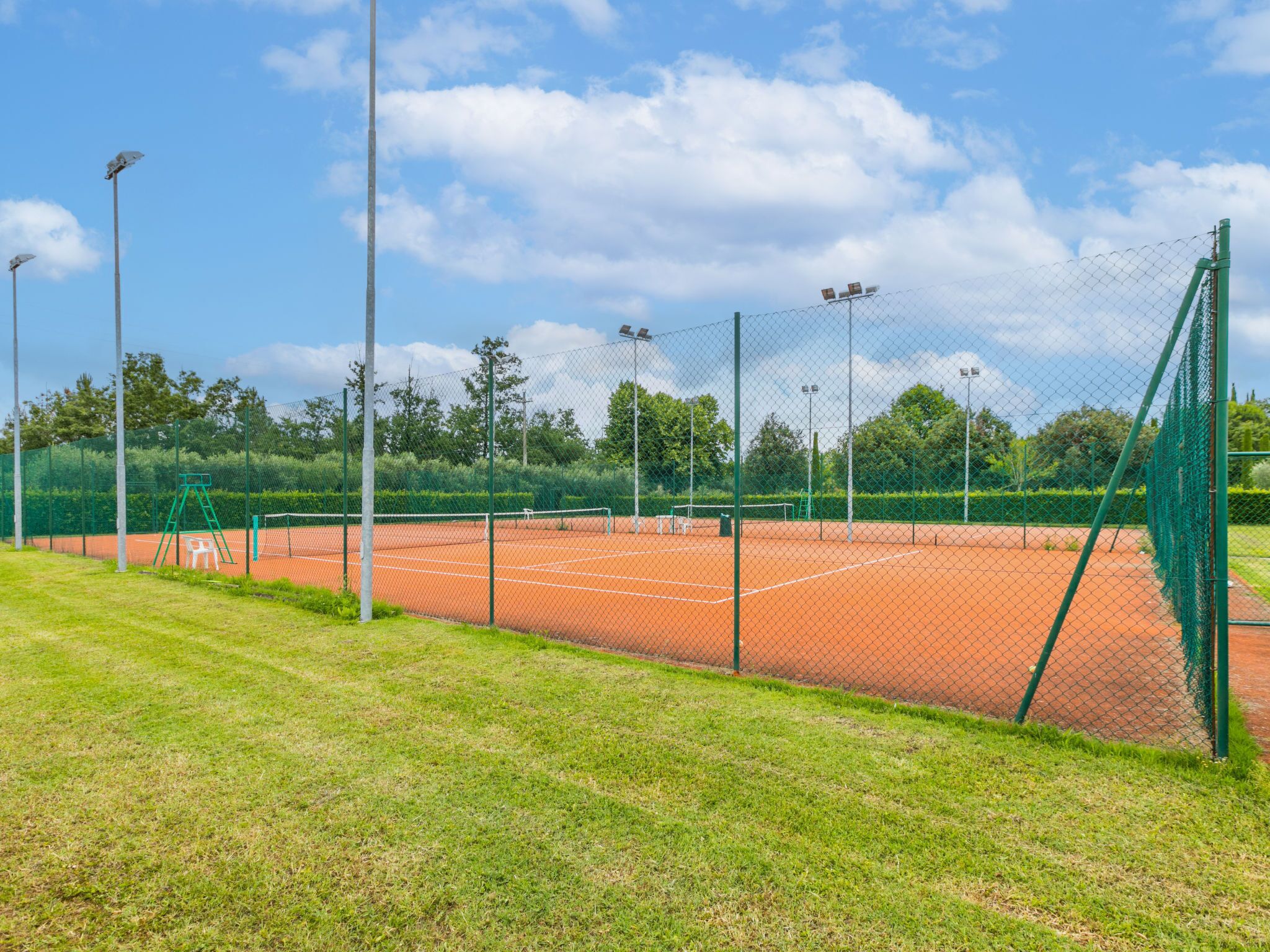 A tennis court with a green fence, a net, and a ladder.