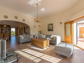 A spacious living room with a sofa, ottoman, and coffee table, a dining area with chairs, and a kitchen visible through an archway.