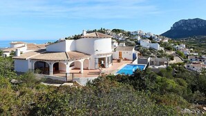 Un villaggio costiero con edifici bianchi, una piscina e una montagna sullo sfondo.