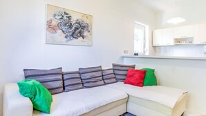 Ein modernes Wohnzimmer mit einer Couch, Kissen, einem Gemälde und einer Küchenzeile.