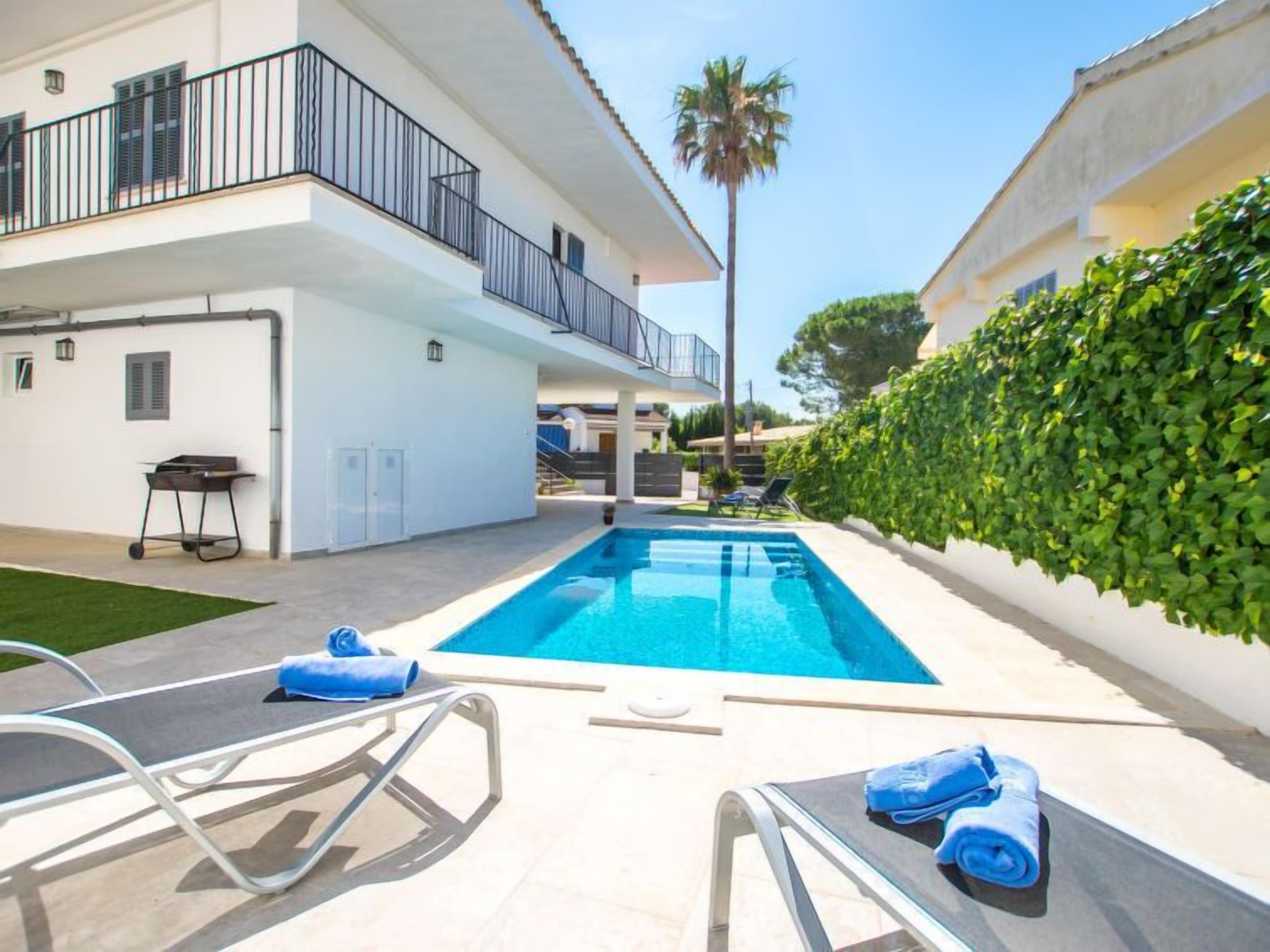 A modern pool area with a clear blue pool, lounge chairs, and a neatly trimmed hedge.