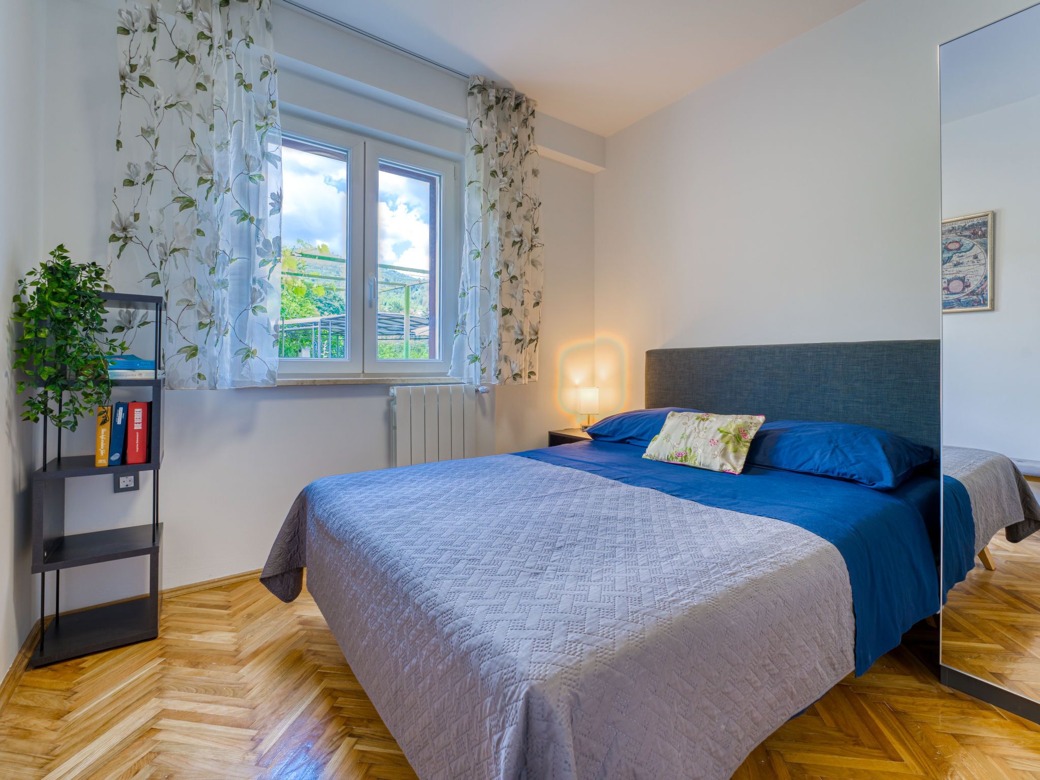 A bedroom with a bed, a nightstand, a bookshelf, a window with curtains, and a radiator.