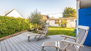 A wooden deck with two lounge chairs, a blue door, and a well-maintained garden.