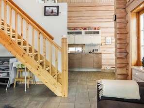 A wooden staircase leading to a kitchen with white cabinets and a dining area with a table and chairs. - Aamunkoi by Interhome (Inari)