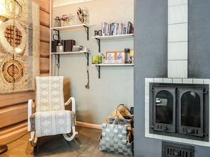 A cozy room with a patterned rug, a white chair, shelves with books and decorative items, and a fireplace. - Aamunkoi by Interhome (Inari)