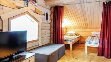 Mukava mökkimainen huone, jossa on televisio, pieni oleskelualue ja kaksi sänkyä.